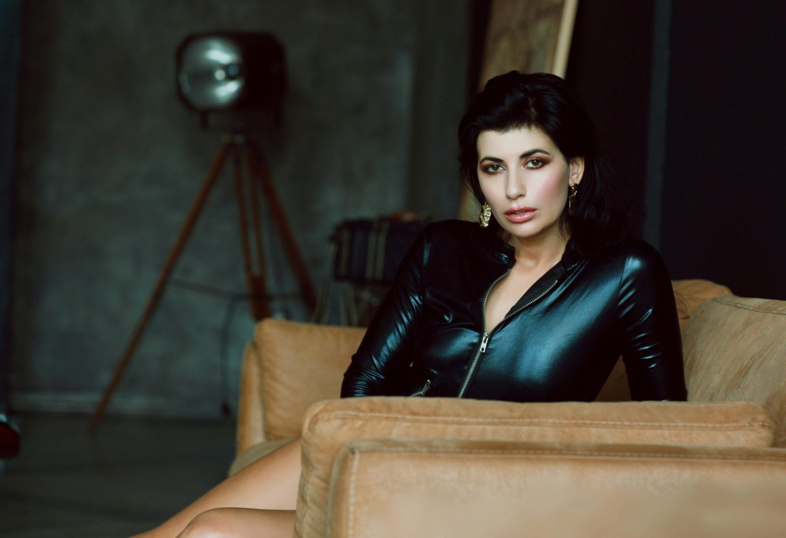 Fashionable woman in a black leather jacket sits on a sofa in a stylish indoor setting.