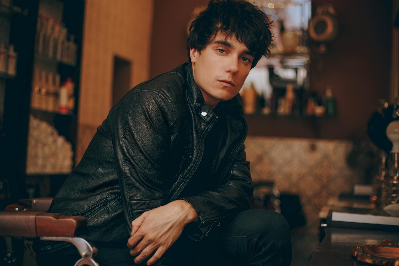 Stylish young man in a black leather jacket posing confidently indoors.